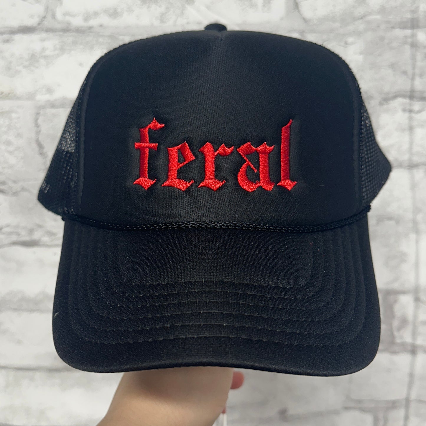 Black mesh trucker hat with red embroidered “feral” text on the front.