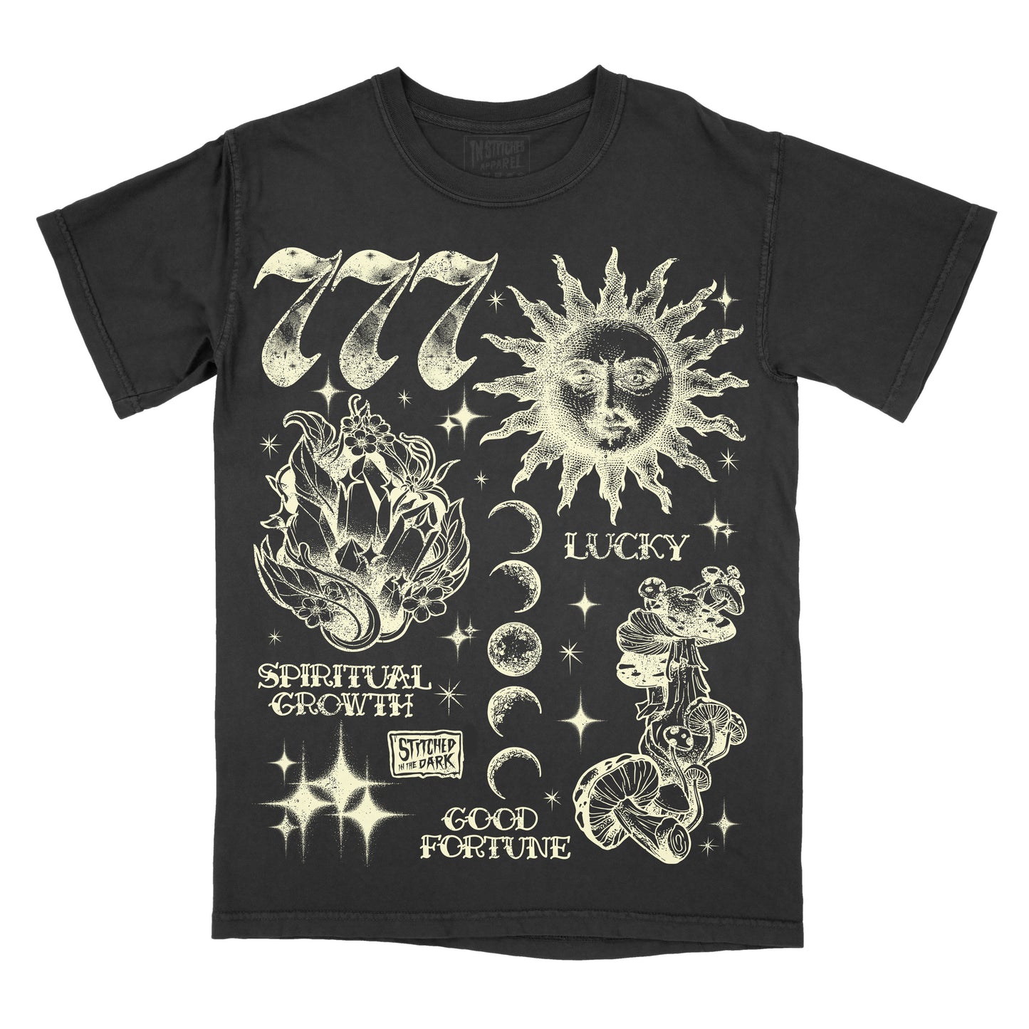 black T-shirt featuring a distressed 777 angel number design with a celestial sun, crystals, moon phases, mushrooms, and stars, with text reading “Lucky,” “Spiritual Growth,” and “Good Fortune,” plus Stitched in the Dark branding.