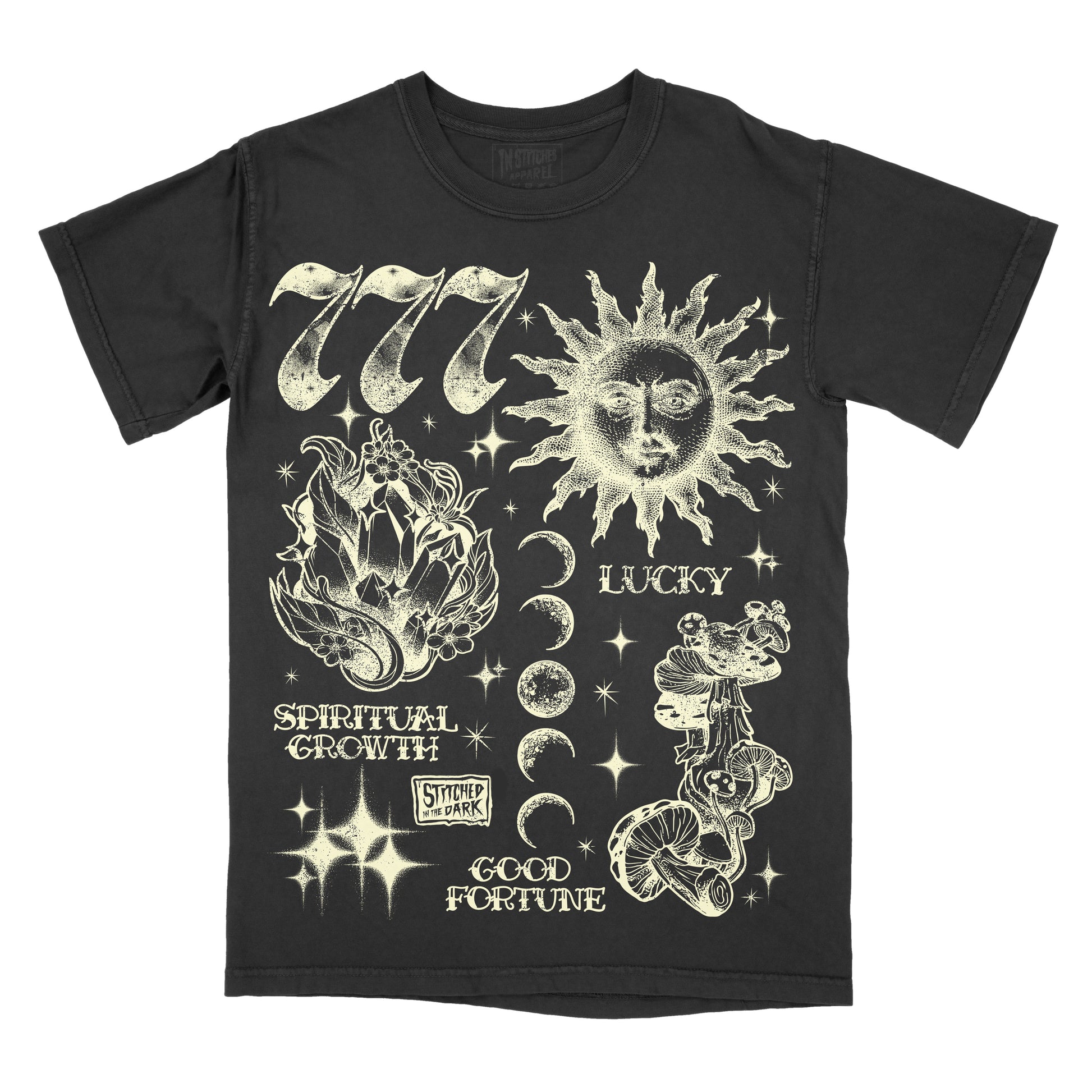 black T-shirt featuring a distressed 777 angel number design with a celestial sun, crystals, moon phases, mushrooms, and stars, with text reading “Lucky,” “Spiritual Growth,” and “Good Fortune,” plus Stitched in the Dark branding.