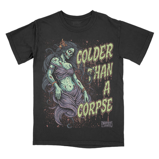 Black garment-dyed graphic t-shirt featuring the phrase "Colder Than a Corpse" alongside an original undead woman illustration with flowing hair, gothic horror styling, and vintage-inspired artwork.
