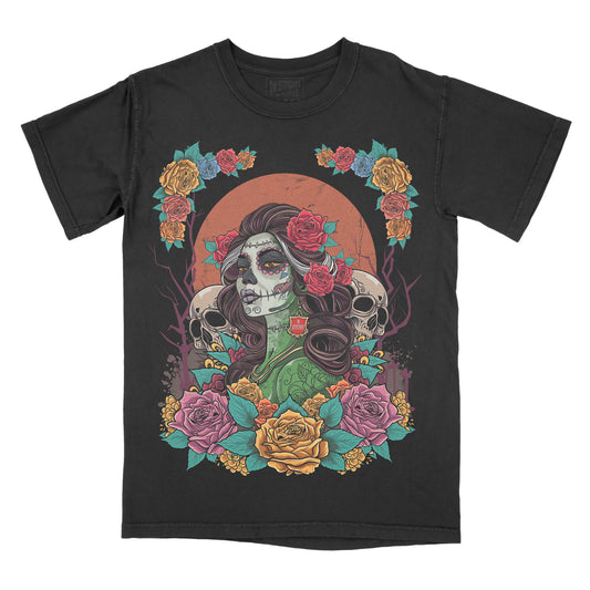 A black short-sleeve t-shirt with a colorful Day of the Dead (Dia de los Muertos) graphic print featuring a sugar skull woman, roses, skulls, and a large orange sun.
