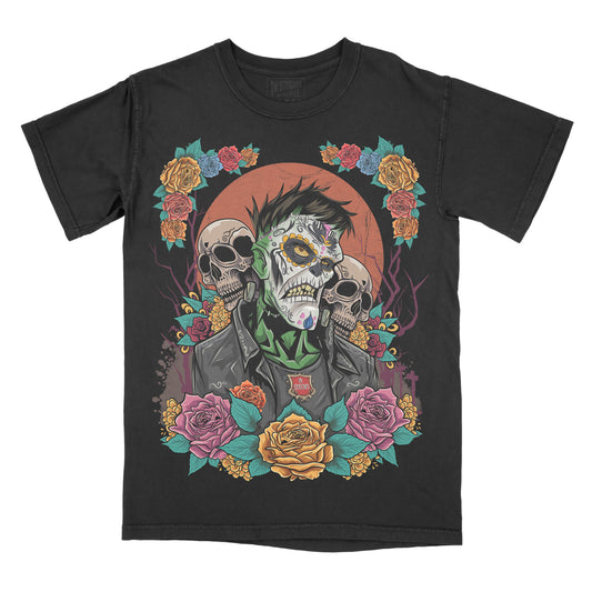 Black garment-dyed graphic t-shirt featuring an original Frankenstein-inspired Day of the Dead design with sugar skull details, colorful floral artwork, and gothic horror aesthetics.