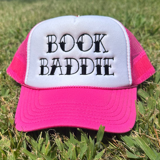 Pink and white foam trucker hat with black embroidered “Book Baddie” design, pink mesh back, pink rope detail, and curved pink bill.