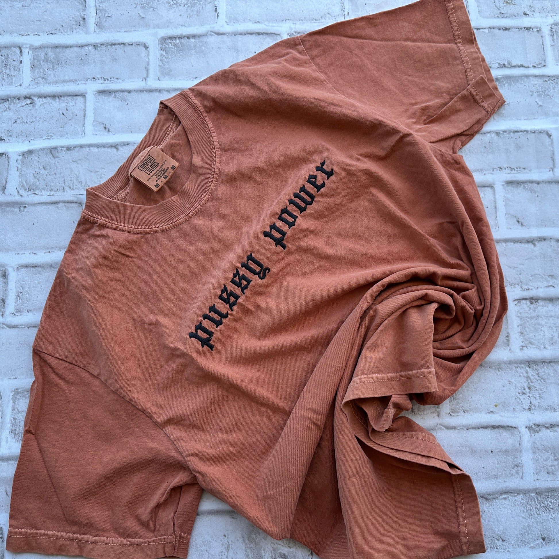 A yam short-sleeve t-shirt with 'pussy power' embroidered in black gothic font across the chest, laid flat against a white background.
