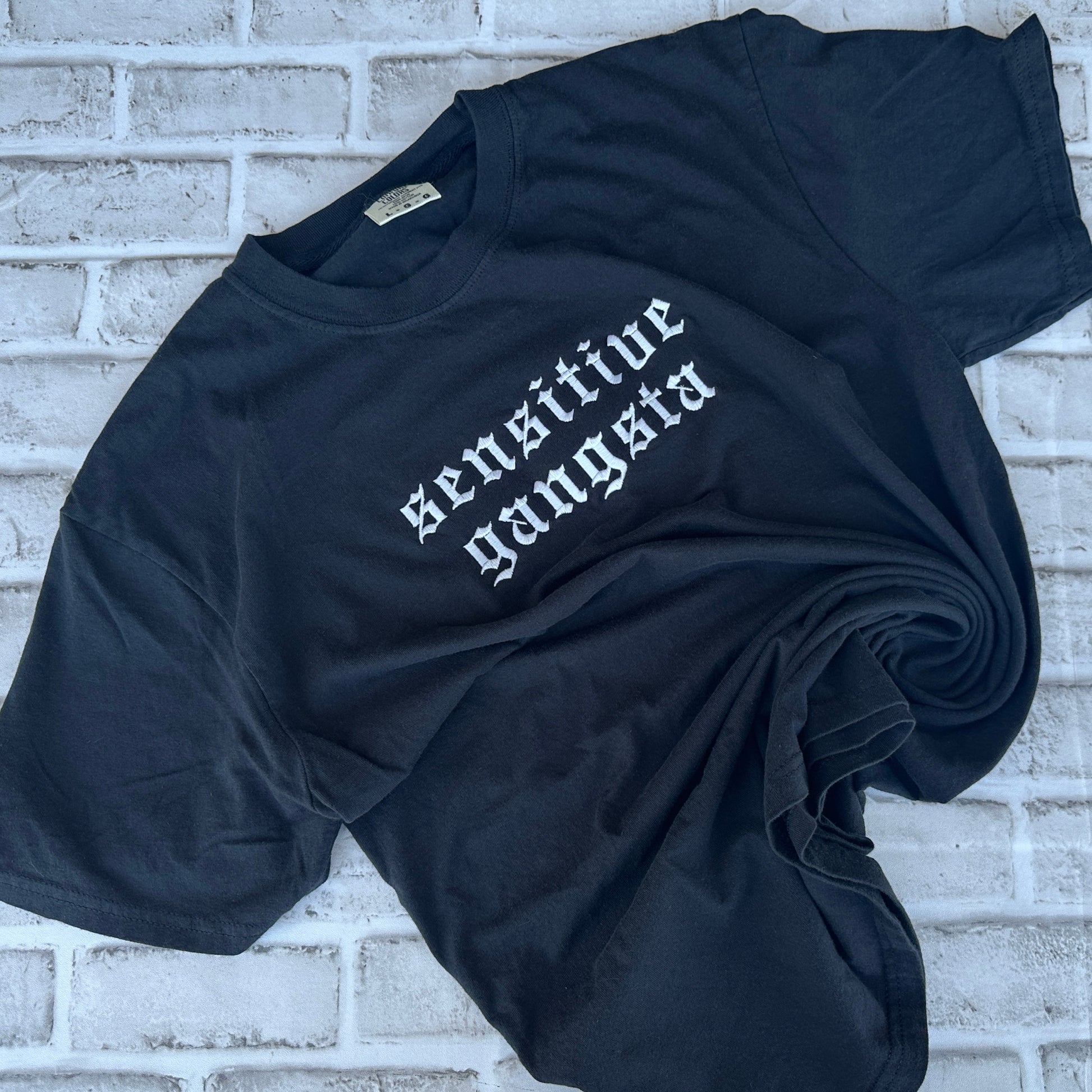 Black Comfort Colors T-shirt featuring white embroidered Old English text across the chest that reads “Sensitive Gangsta.”