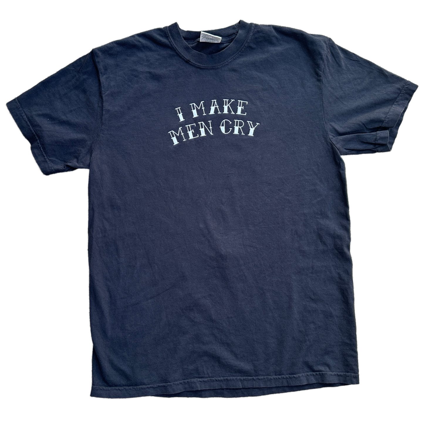 A black short-sleeve t-shirt with the phrase 'I MAKE MEN CRY' embroidered in a distressed white font across the chest, laid flat against a white background.