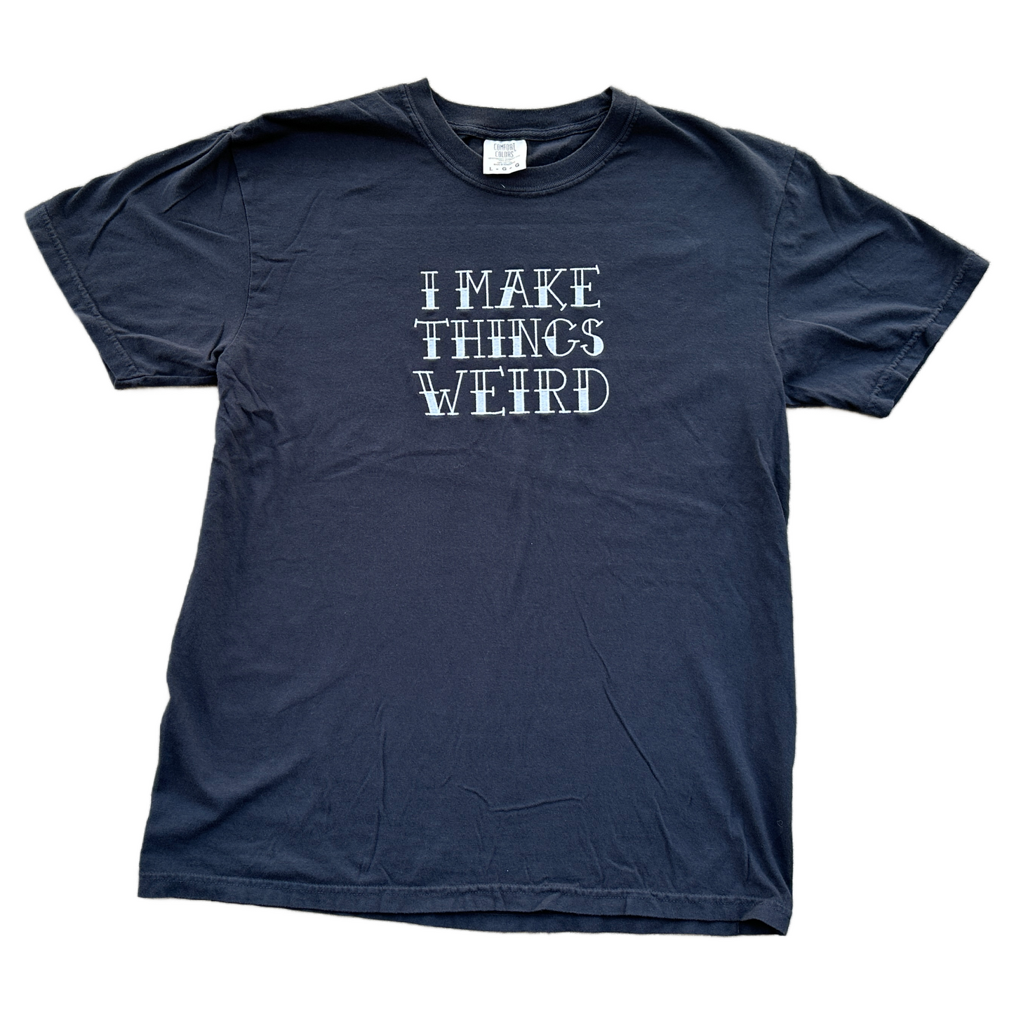 A black short-sleeve t-shirt with the phrase 'I MAKE THINGS WEIRD' embroidered in white letters across the chest, laid flat against a white background.