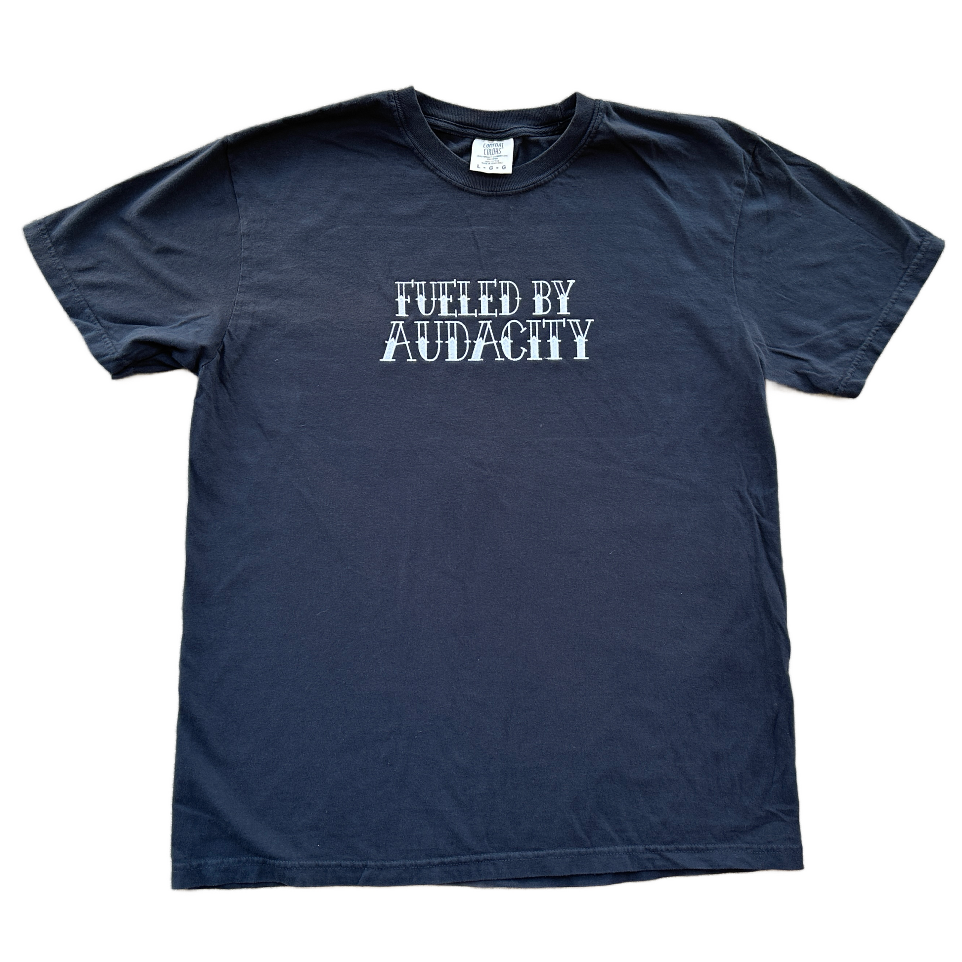 A black short-sleeve t-shirt with the phrase 'FUELED BY AUDACITY' embroidered in a distressed white font across the chest, displayed flat against a white background.