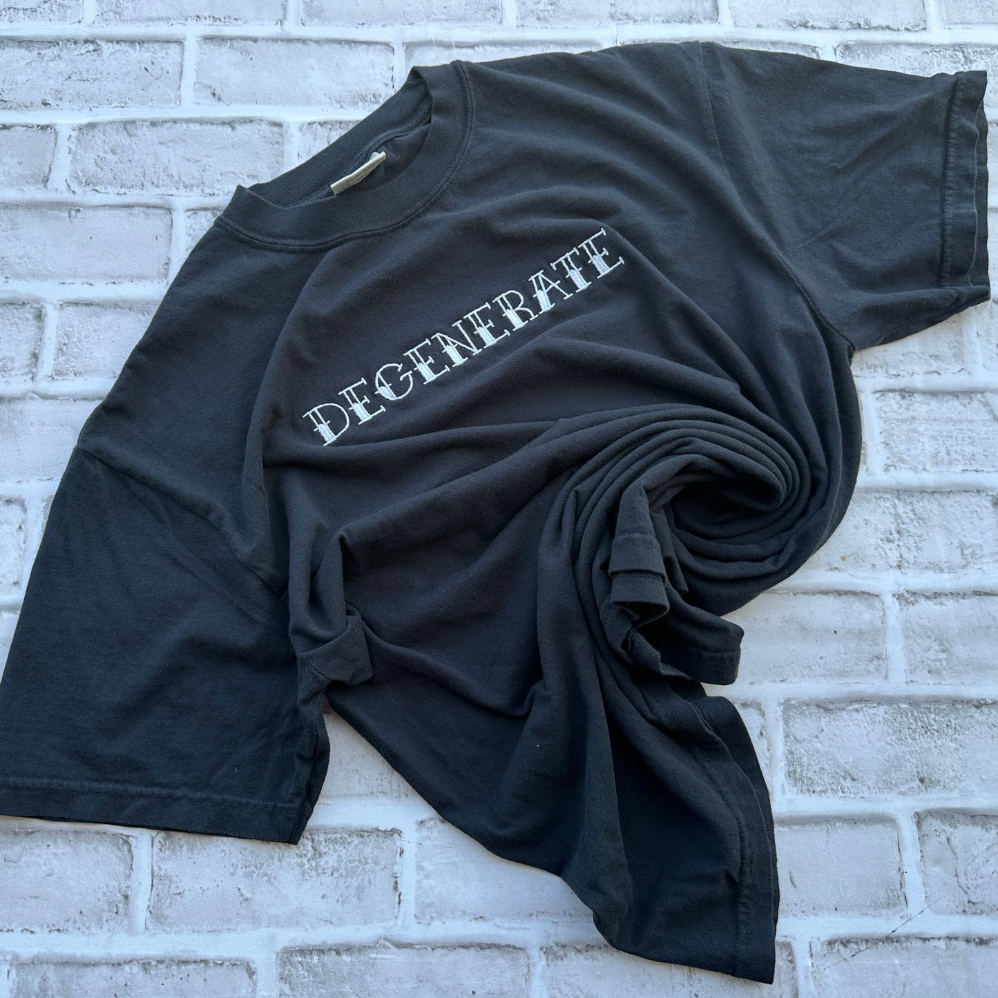 A black short-sleeve t-shirt with the word 'DEGENERATE' embroidered in white letters across the chest, laid flat against a white background.