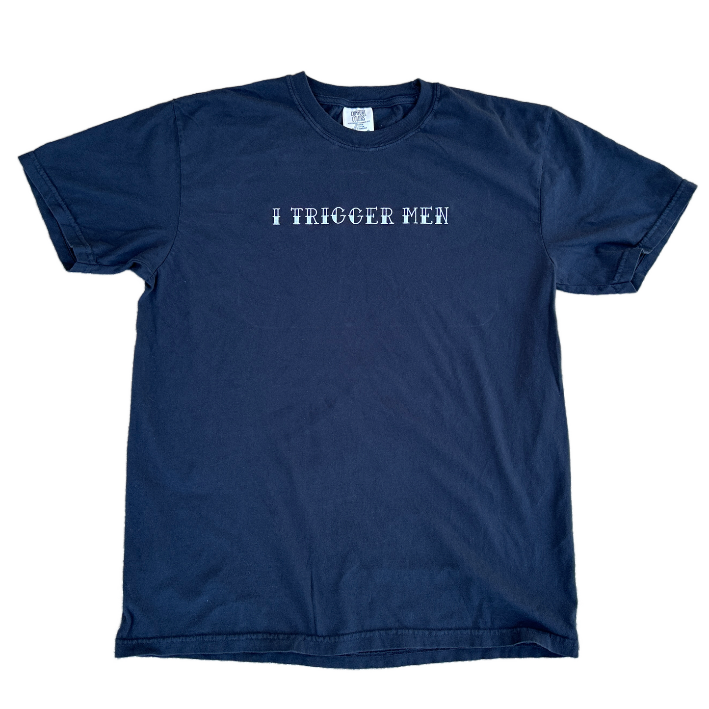 A black short-sleeve crewneck t-shirt with the text 'I TRIGGER MEN' embroidered in white across the chest, displayed flat against a white background.