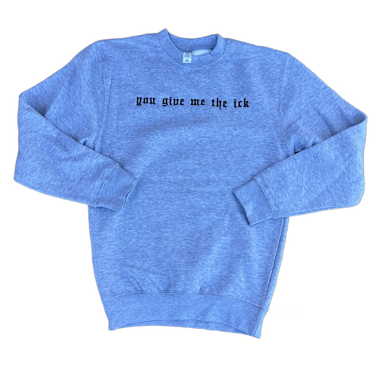 A heather grey crewneck sweatshirt with the phrase 'you give me the ick' embroidered across the chest in a black gothic font, displayed flat against a white background.