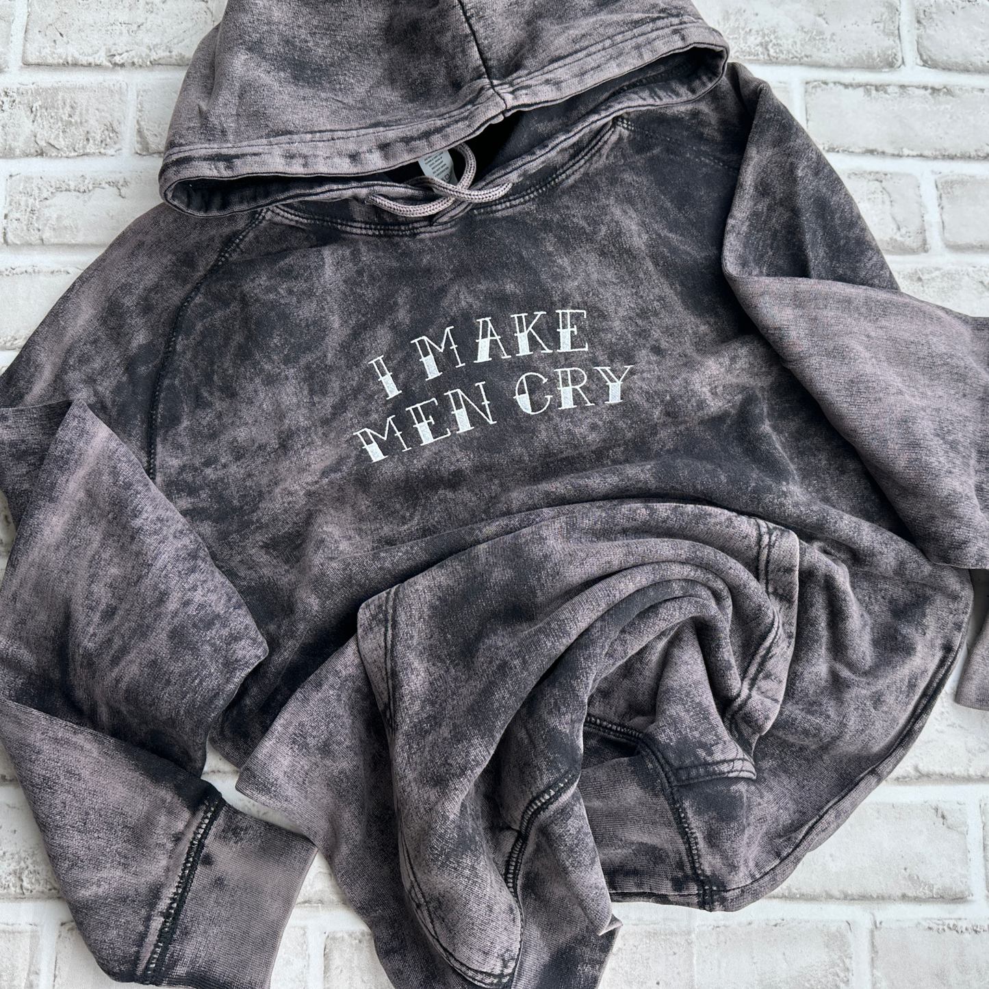 Vintage cloud black mineral-washed hoodie featuring white embroidered text across the chest that reads “I Make Men Cry,” with a front kangaroo pocket and drawstring hood.