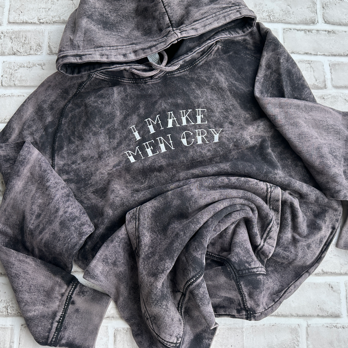 Vintage cloud black mineral-washed hoodie featuring white embroidered text across the chest that reads “I Make Men Cry,” with a front kangaroo pocket and drawstring hood.