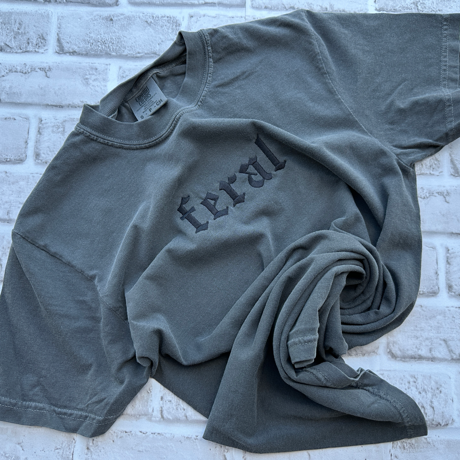 A pepper embroidered t-shirt with the word 'feral' written in bold letters across the front.