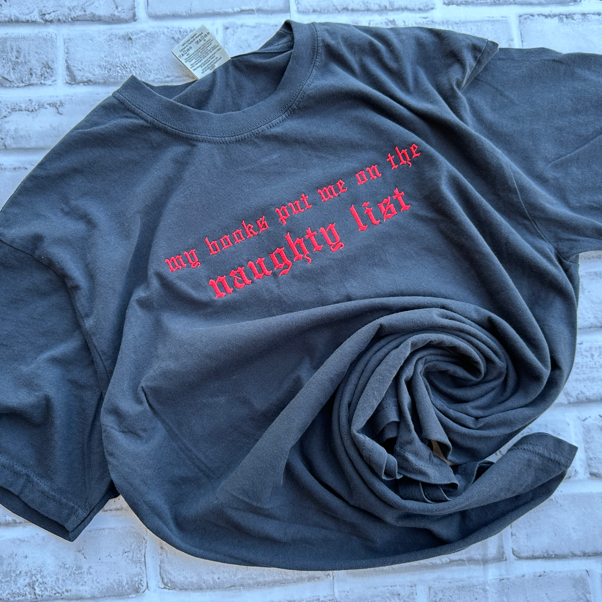 Black Comfort Colors T-shirt featuring bright red embroidered Old English text across the chest that reads “my books put me on the naughty list.