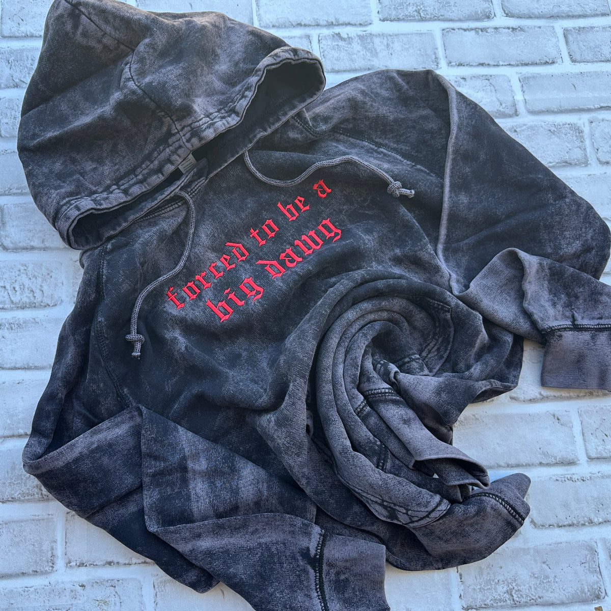 Black mineral-washed pullover hoodie featuring red Old English embroidered text across the chest reading “forced to be a big dawg,” with drawstring hood, front kangaroo pocket, and distressed vintage wash.