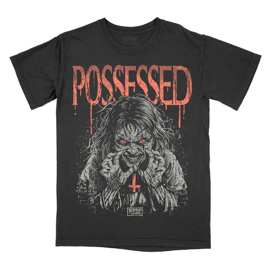 A black short-sleeve graphic t-shirt featuring a distressed red 'POSSESSED' text and a horror-themed illustration of a creepy figure with red eyes and a red cross on the chest, set against a plain white background.