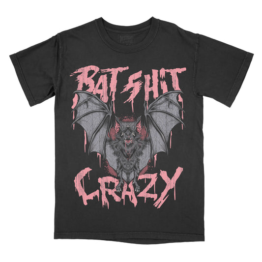 A black short-sleeve t-shirt with a graphic of a bat in the center, flanked by dripping pink text reading 'BAT SHIT' above and 'CRAZY' below, shown on a plain white background.