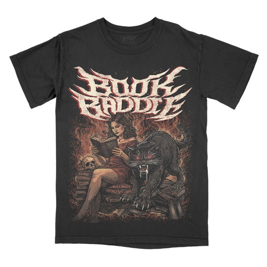 A black graphic t-shirt featuring the text 'Book Baddie' in a stylized white and red font above an illustration of a woman reading, a large black cat, and a skull on a fiery background.