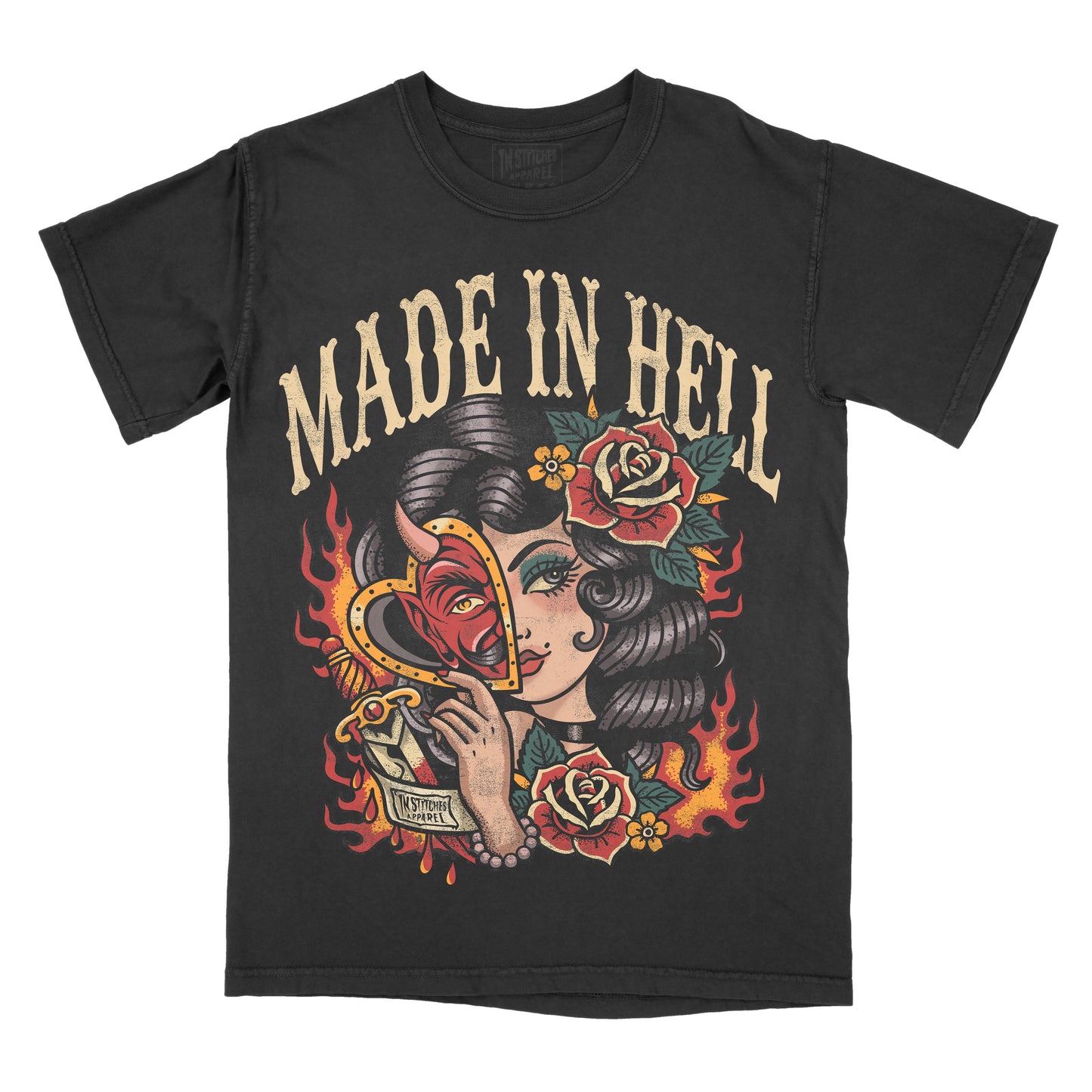 Black Comfort Colors graphic T-shirt featuring a vintage tattoo-style illustration of a woman holding a devil heart mask with roses, flames, and the phrase "Made in Hell."