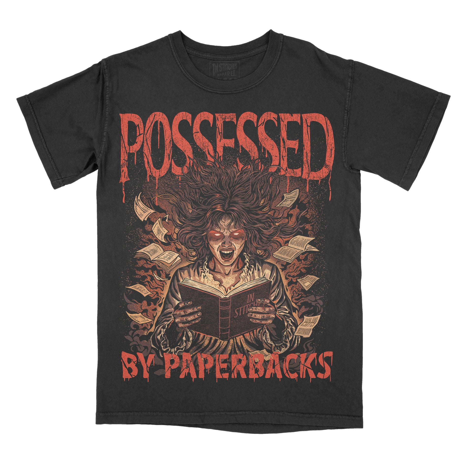 A black short-sleeve graphic t-shirt featuring a horror illustration of a screaming woman reading a book surrounded by books, with the text 'POSSESSED BY PAPERBACKS' in a dripping red font.