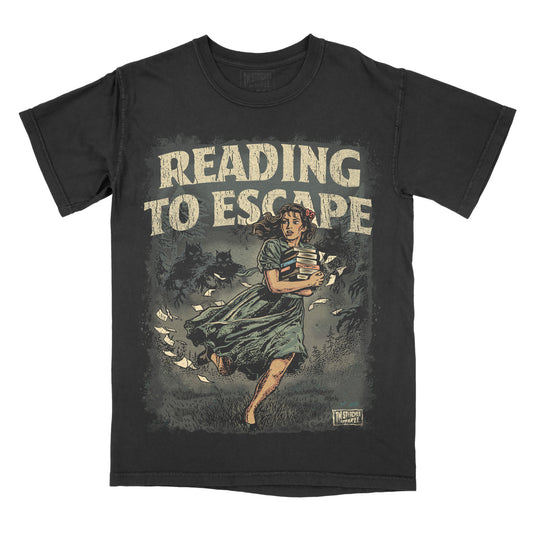 Black garment-dyed graphic t-shirt featuring the phrase "Reading to Escape" with an original vintage-inspired illustration of a woman carrying books while fleeing shadowy monsters through a dark forest.