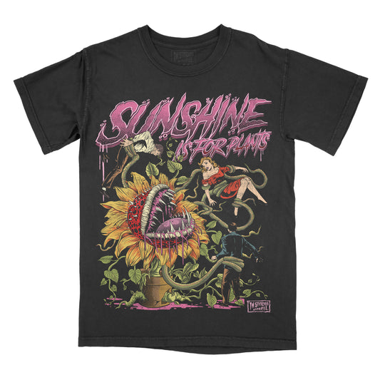 A black short-sleeve graphic t-shirt featuring a detailed horror illustration of a giant sunflower with a screaming mouth, green vines, a girl in a red dress, and the text 'SUNSHINE IS FOR PLANTS' in dripping pink lettering.